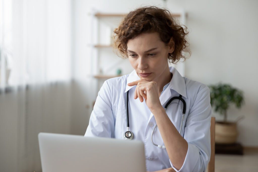 Concentrated young female physician working on computer doing online research